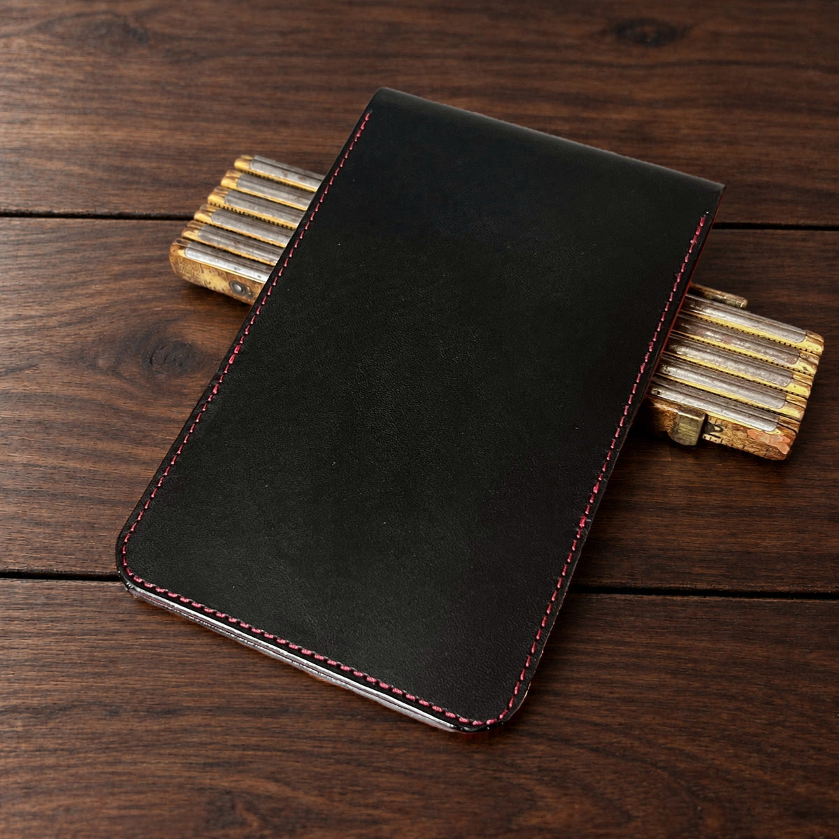 Augusta Classic leather yardage book cover in Black Buttero with red thread, closed, on a wood table with pencils