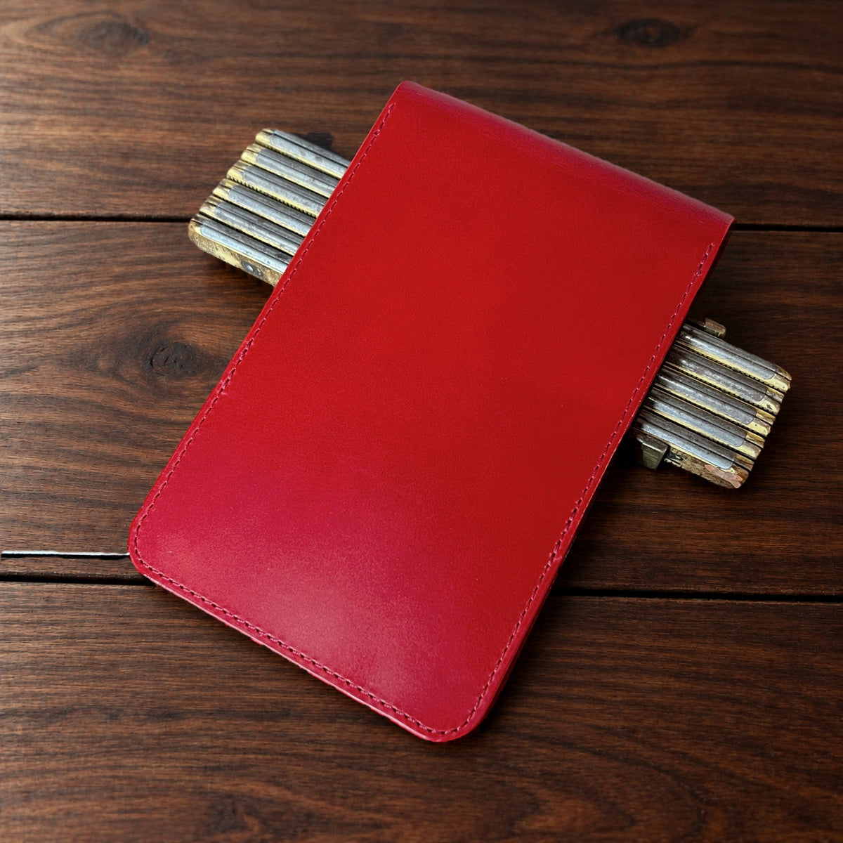 Augusta Classic leather yardage book cover in Red Buttero with red thread, closed, on a wood table with pencils