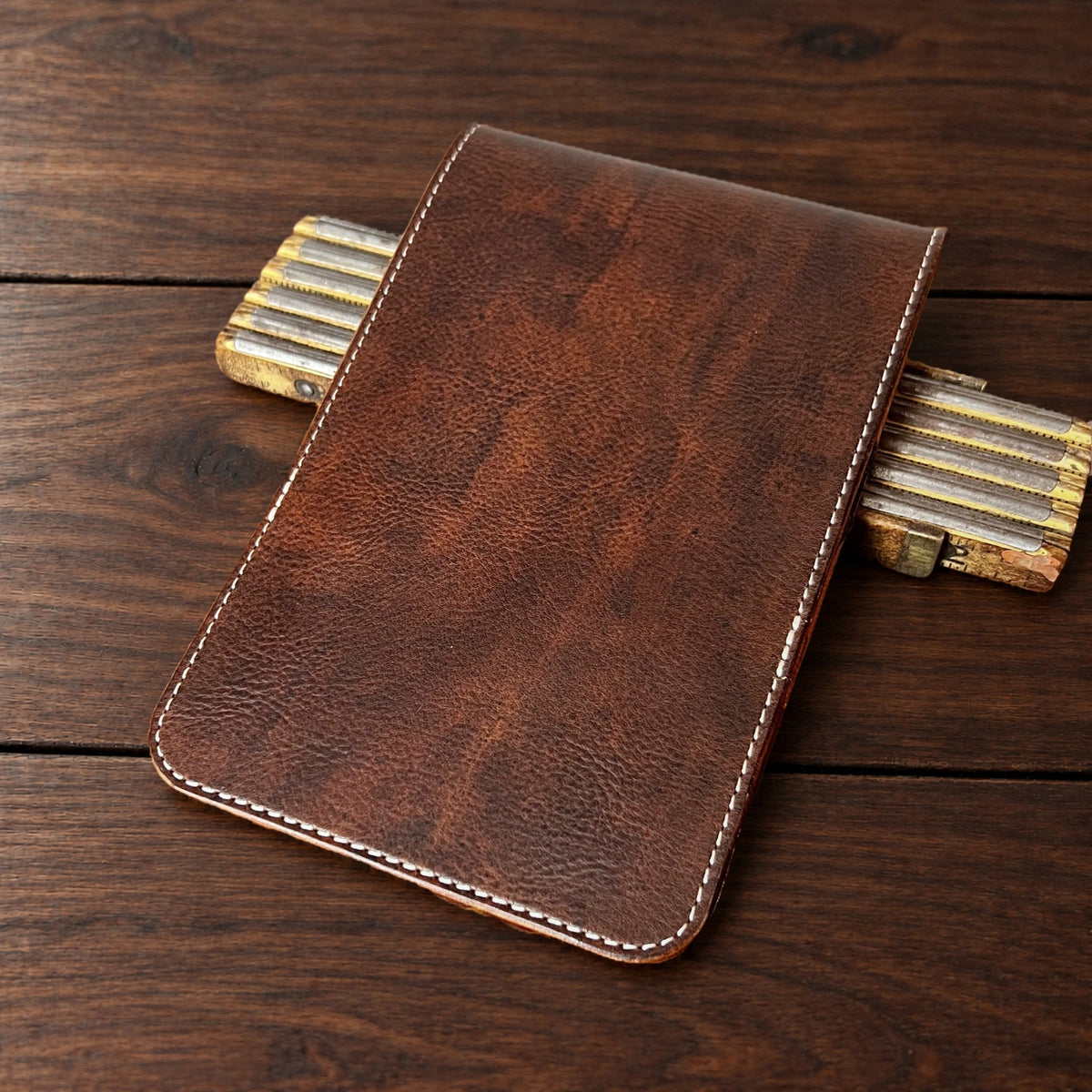 Augusta Classic leather yardage book cover in Nemesis with cream thread, closed, on a wood table with pencils