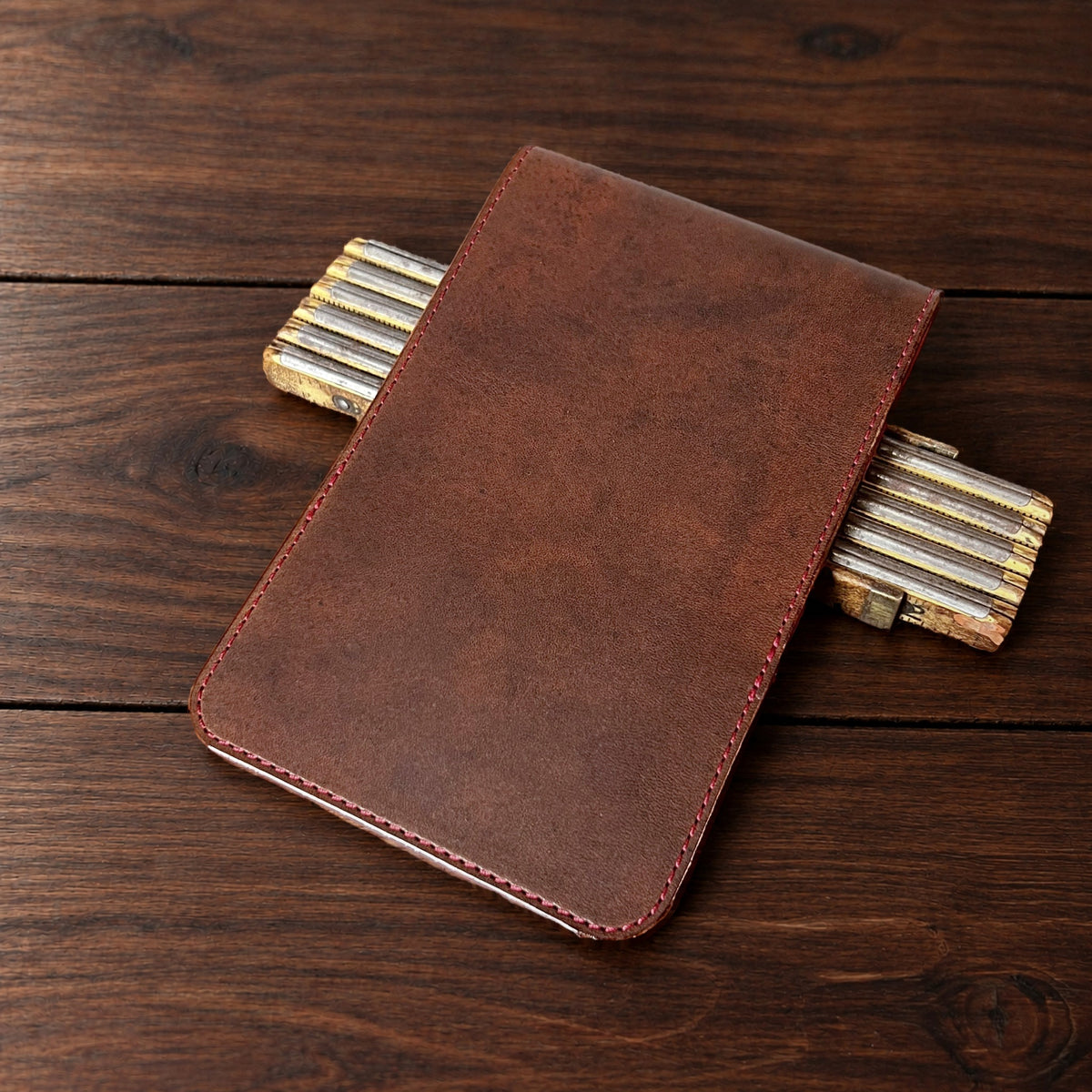 Augusta Classic leather yardage book cover in Nemesis with red thread, closed, on a wood table with pencils