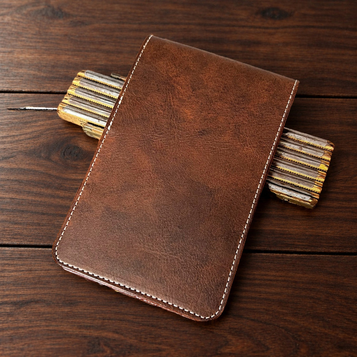 Augusta Classic leather yardage book cover in Nemesis with cream thread, closed, on a wood table with pencils
