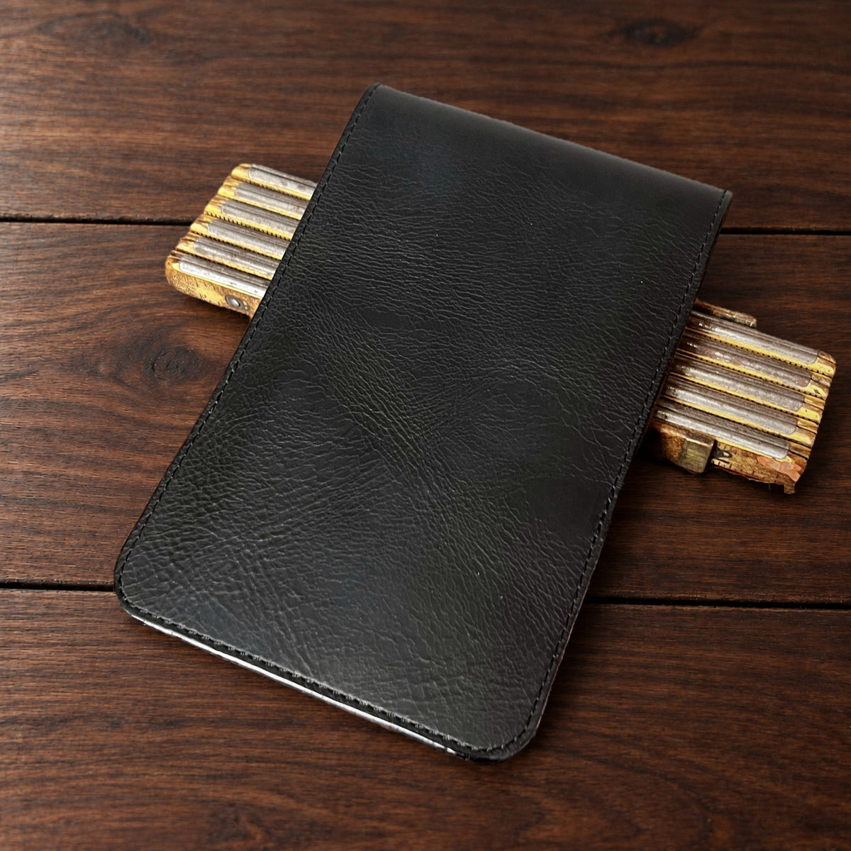 Augusta Classic leather yardage book cover in Black Waxy with black thread, closed, on a wood table with pencils