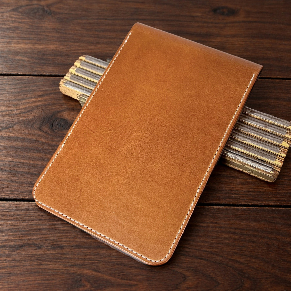 Augusta Classic leather yardage book cover in Whiskey Buttero with cream thread, closed, on a wood table with pencils
