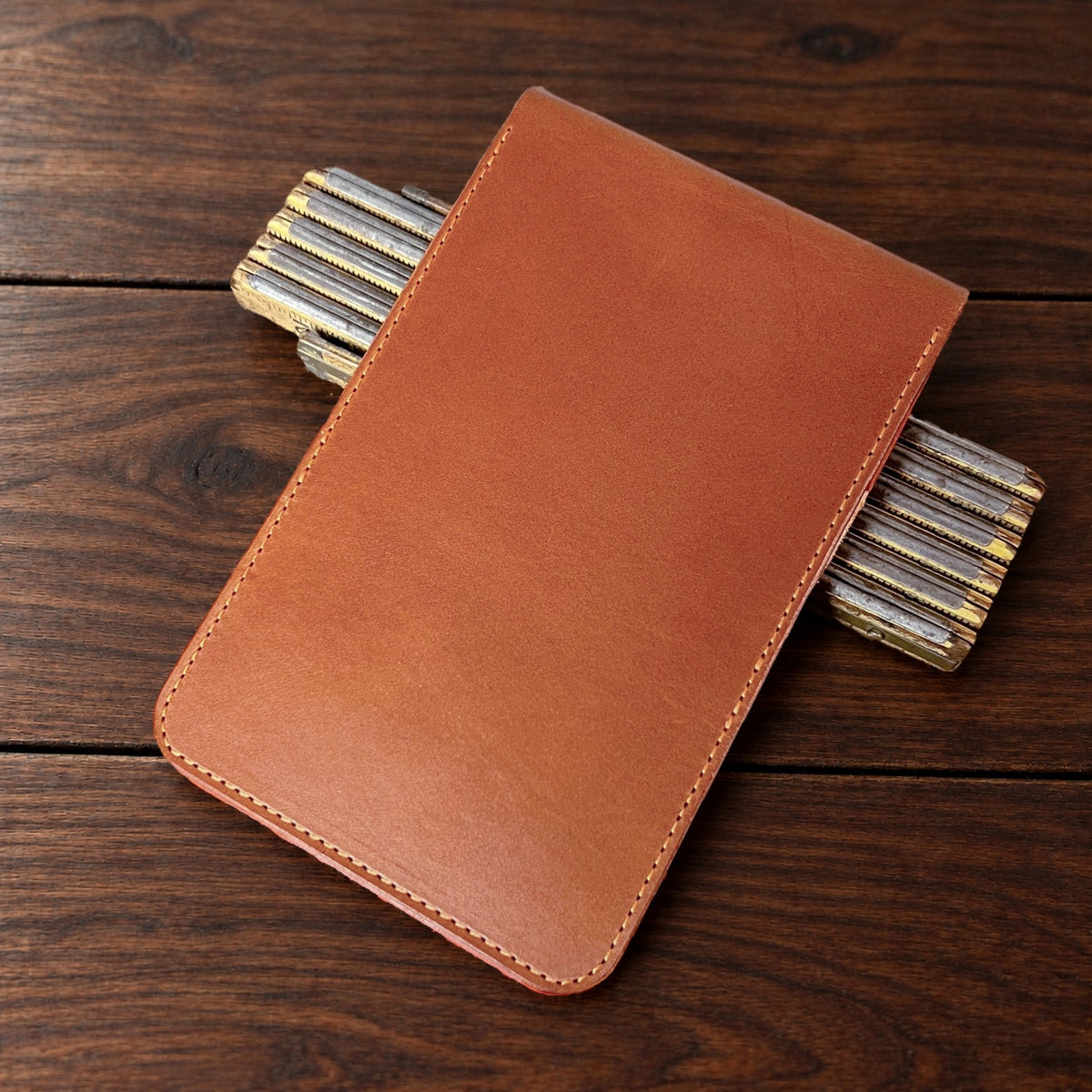 Oakmont Classic leather yardage book cover in Whiskey Buttero with orange thread, closed, on a wood table with pencils