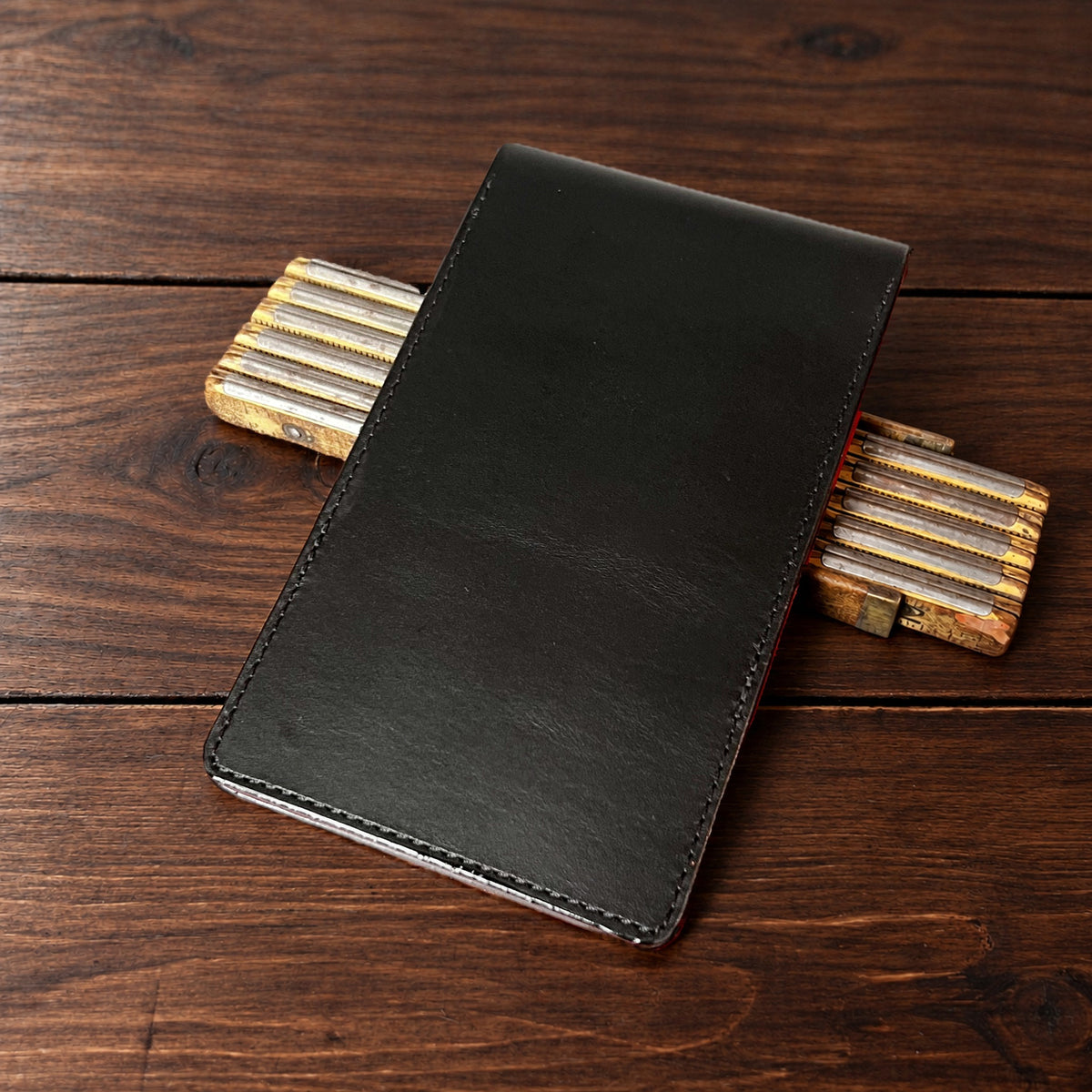 Augusta Pro leather yardage book cover in Black Buttero with black thread, closed, on a wood table with pencils