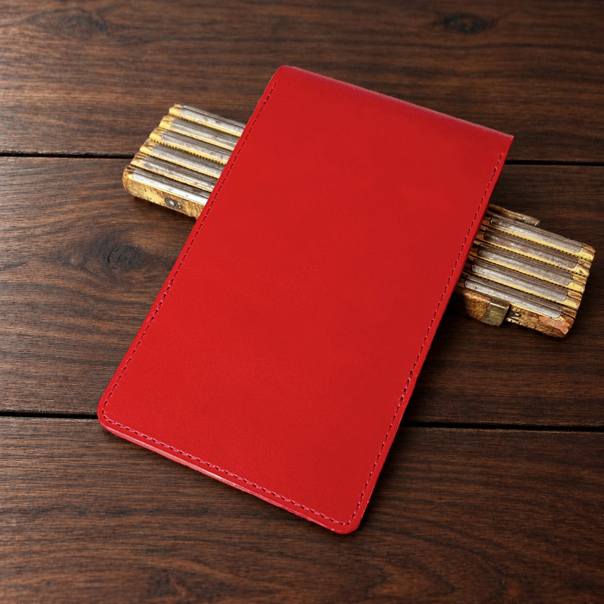 Augusta Pro leather yardage book cover in Red Buttero with red thread, closed, on a wood table with pencils