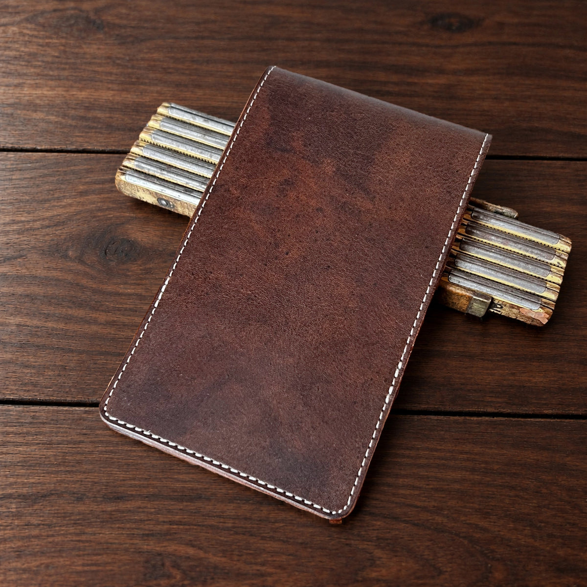 Augusta Pro leather yardage book cover in Nemesis with cream thread, closed, on a wood table with pencils