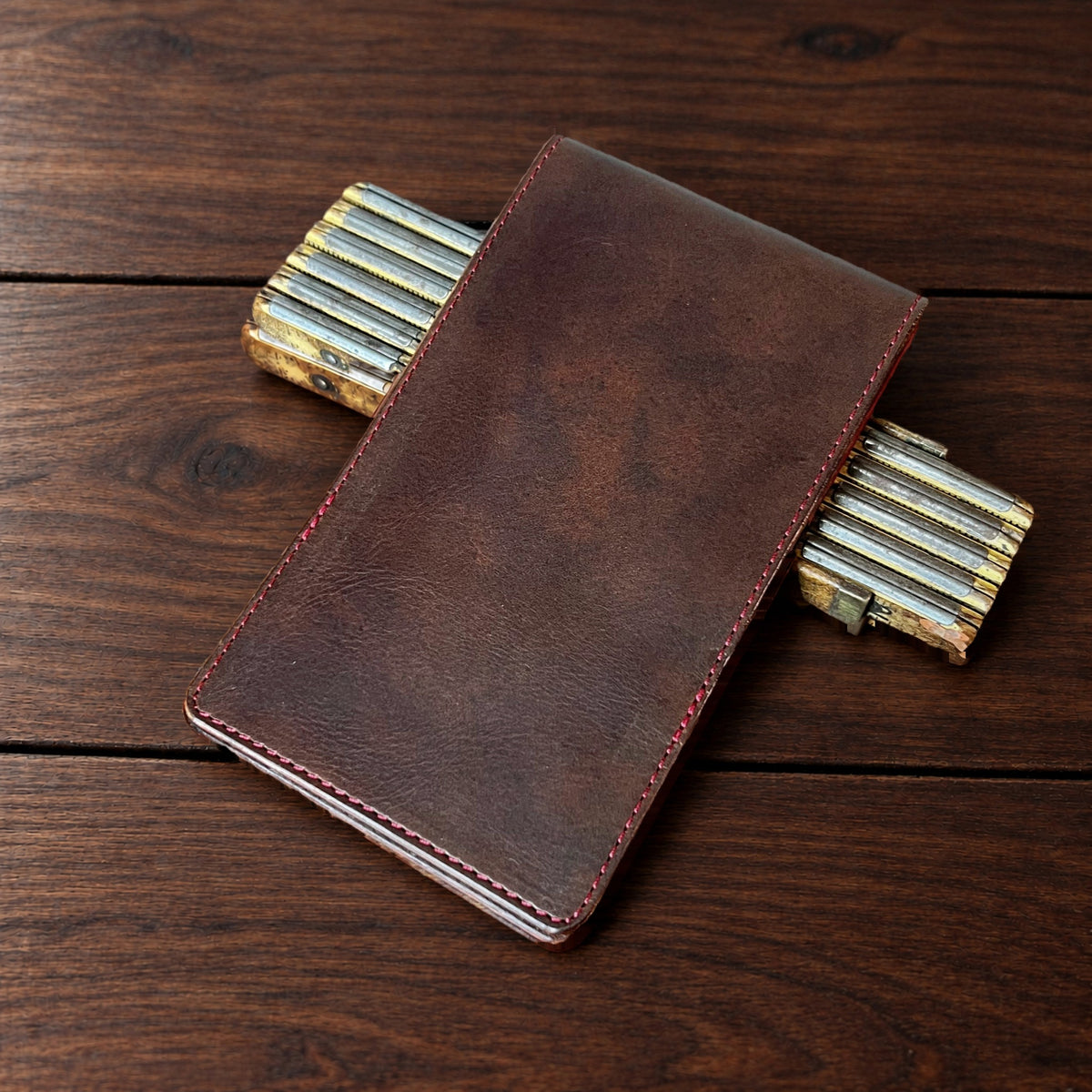 Augusta Pro leather yardage book cover in Nemesis with red thread, closed, on a wood table with pencils