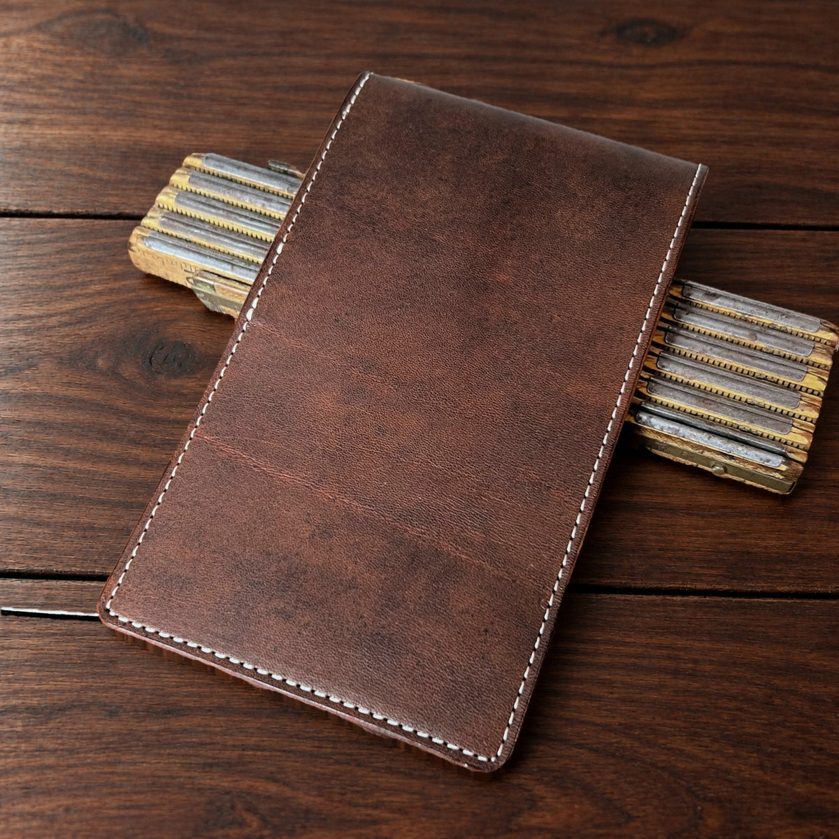Augusta Pro leather yardage book cover in Nemesis with cream thread, closed, on a wood table with pencils