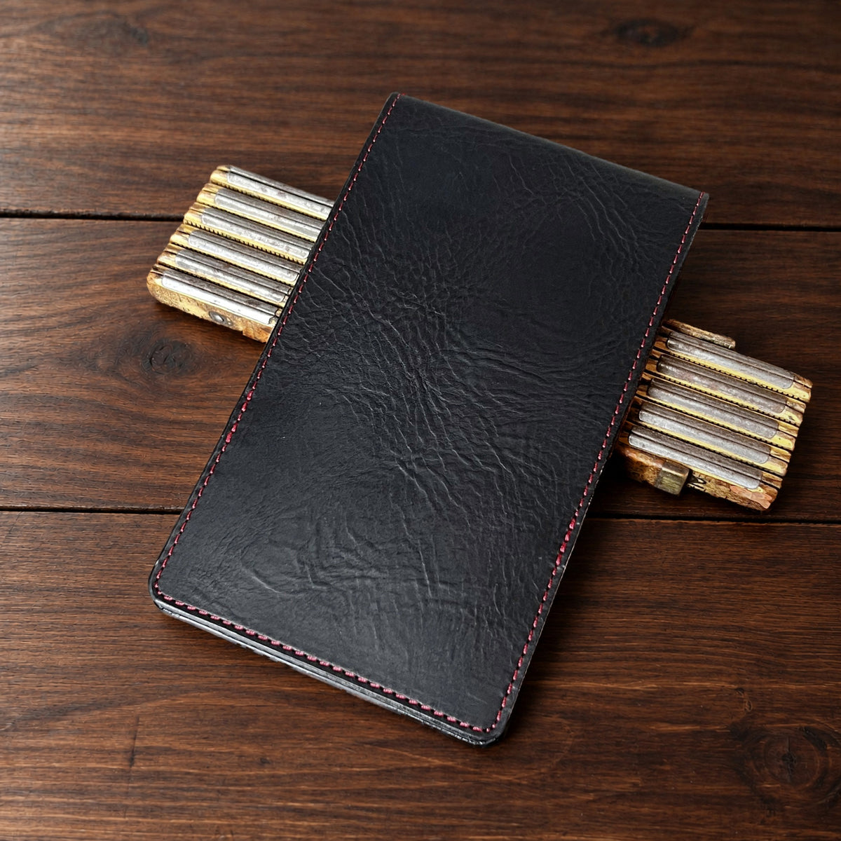 Augusta Pro leather yardage book cover in Black Waxy with black thread, closed, on a wood table with pencils