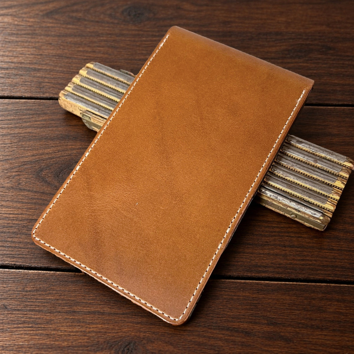 Augusta Pro leather yardage book cover in Whiskey Buttero with cream thread, closed, on a wood table with pencils