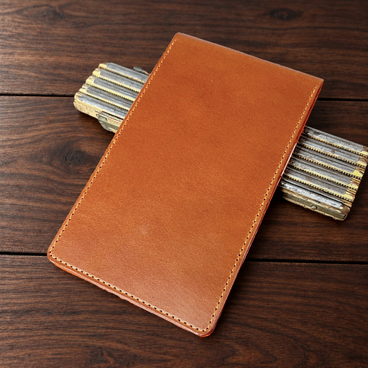 Oakmont Pro leather yardage book cover in Whiskey Buttero with orange thread, closed, on a wood table with pencils