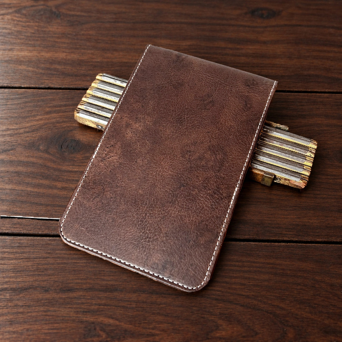 Oakmont Classic leather yardage book cover in Nemesis with cream thread, closed, on a wood table with pencils
