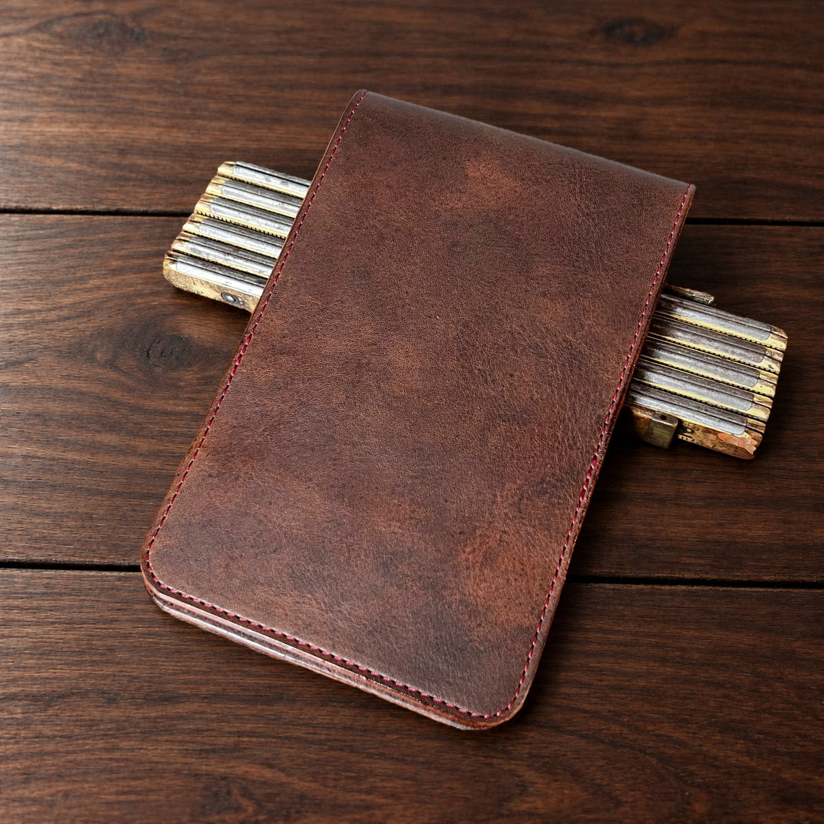 Oakmont Classic leather yardage book cover in Nemesis with red thread, closed, on a wood table with pencils