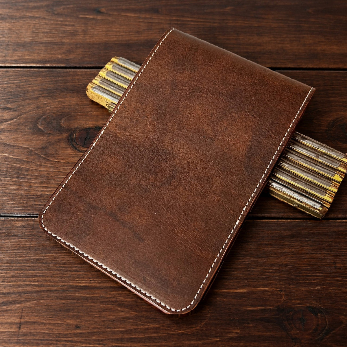 Oakmont Classic leather yardage book cover in Nemesis with cream thread, closed, on a wood table with pencils