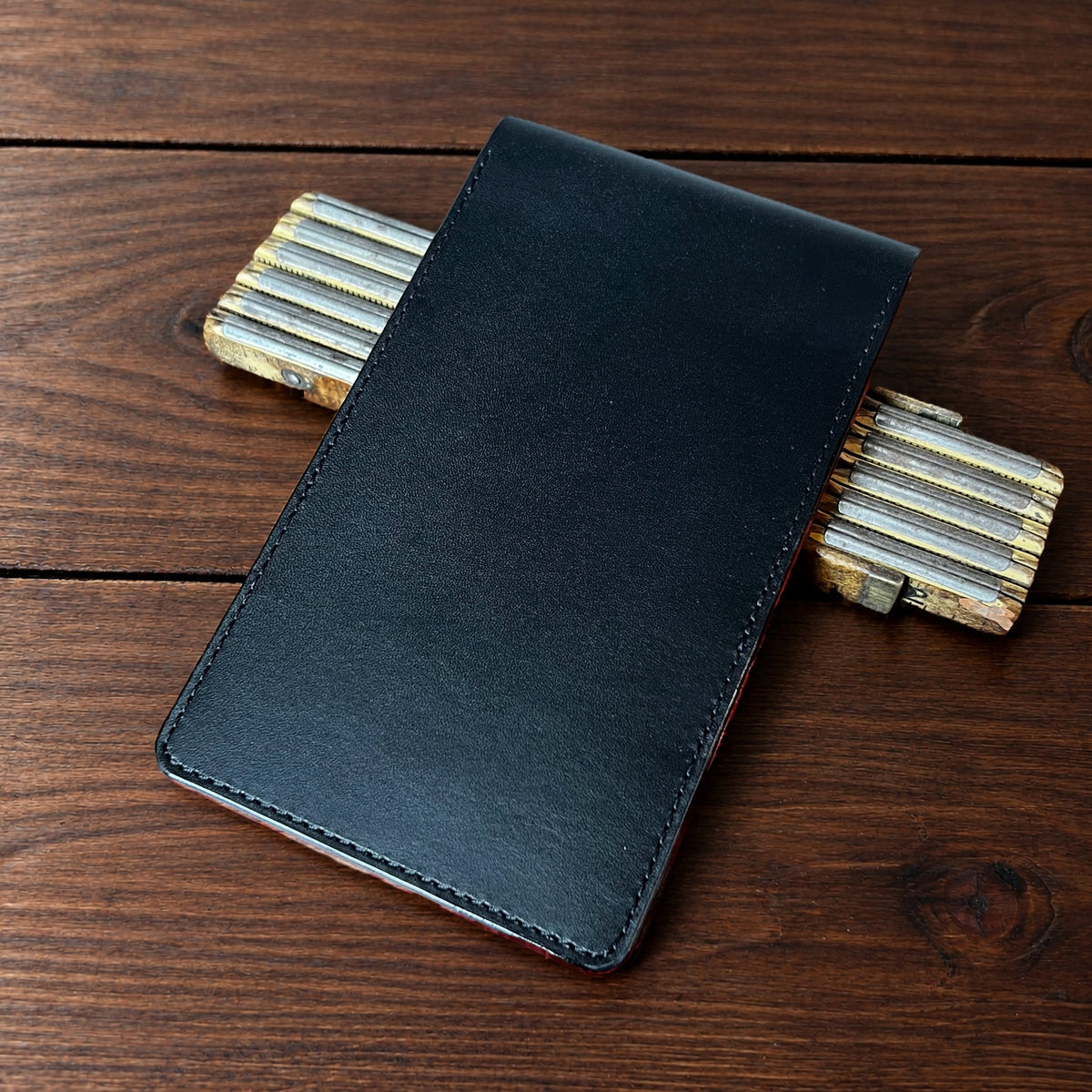 Oakmont Pro leather yardage book cover in Black Buttero with black thread, closed, on a wood table with pencils