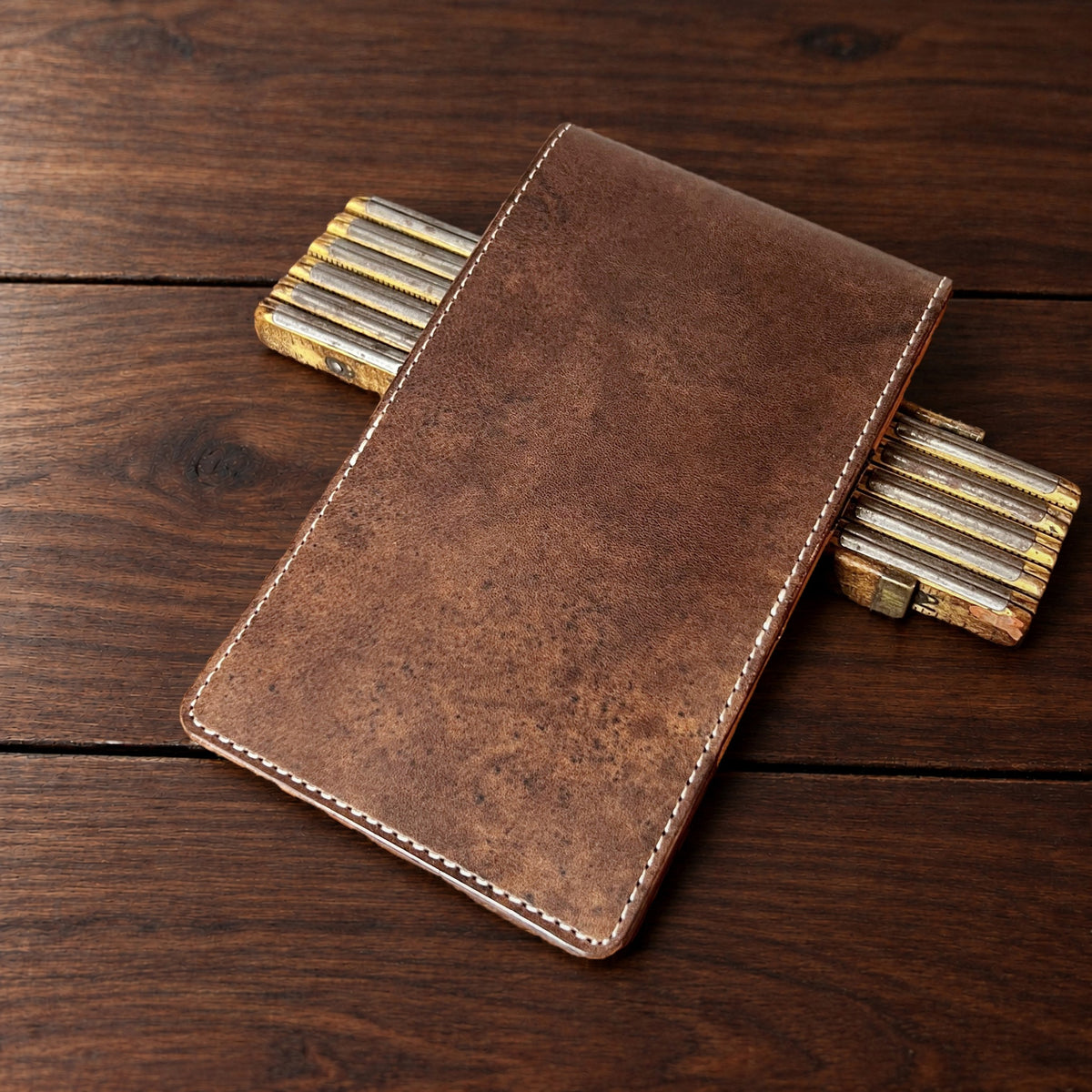 Oakmont Pro leather yardage book cover in Nemesis with cream thread, closed, on a wood table with pencils