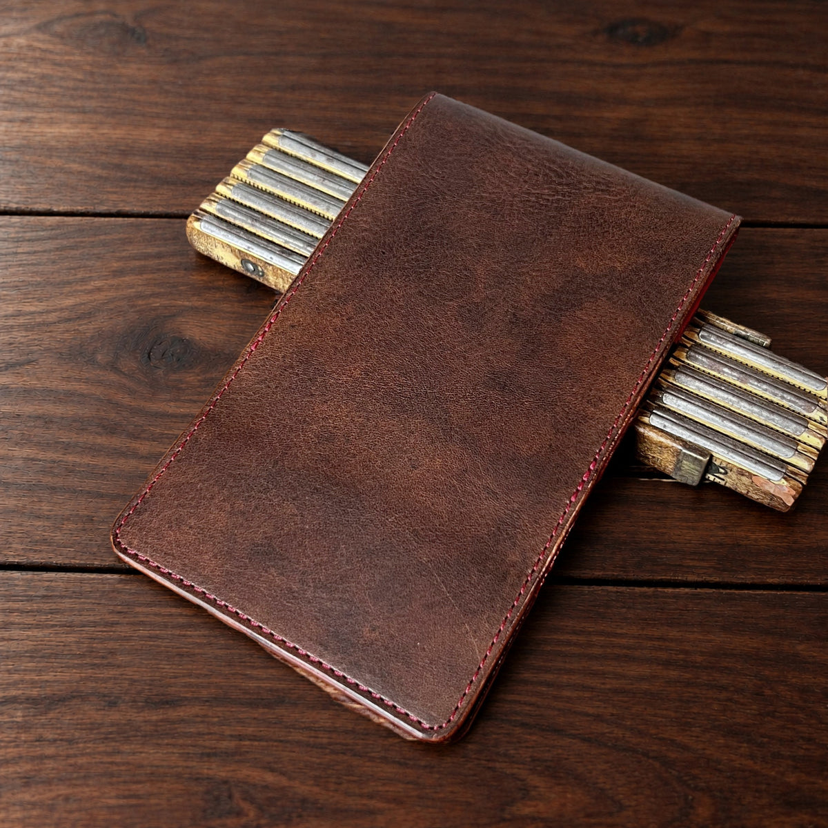 Oakmont Pro leather yardage book cover in Nemesis with red thread, closed, on a wood table with pencils