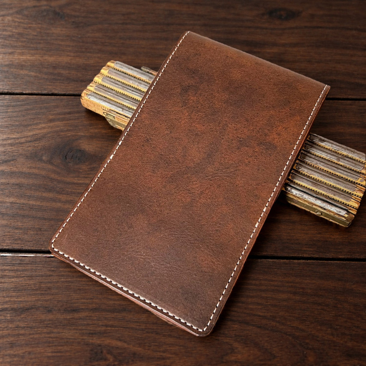 Oakmont Pro leather yardage book cover in Nemesis with cream thread, closed, on a wood table with pencils