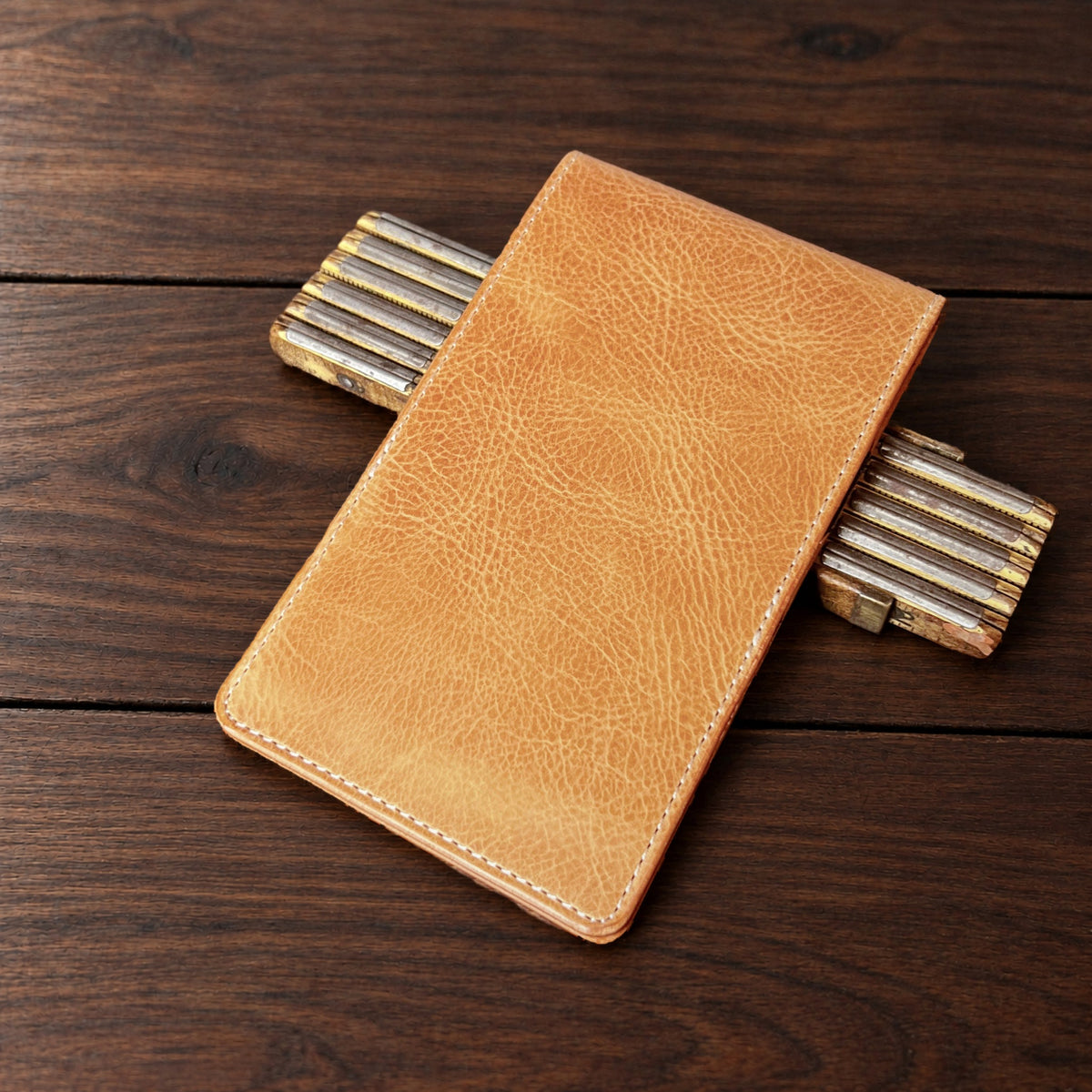 Oakmont Pro leather yardage book cover in Natural Waxy with cream thread, closed, on a wood table with pencils