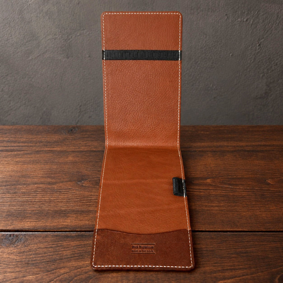 Inside of an open Augusta yardage book cover standing on a walnut table: a top elastic, a full-length bottom pocket and a pencil loop
