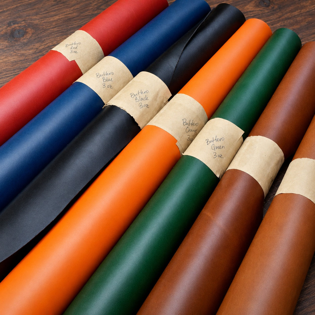 Rolls of Buttero leather in red, blue, black, orange, green and browns with handwritten kraft paper labels, on a walnut bench