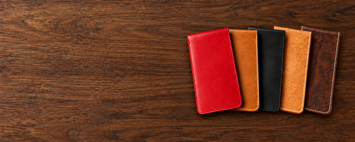 Five leather yardage book covers in red, whiskey and black Buttero, natural Waxy and Nemesis, laid in a row on a walnut table