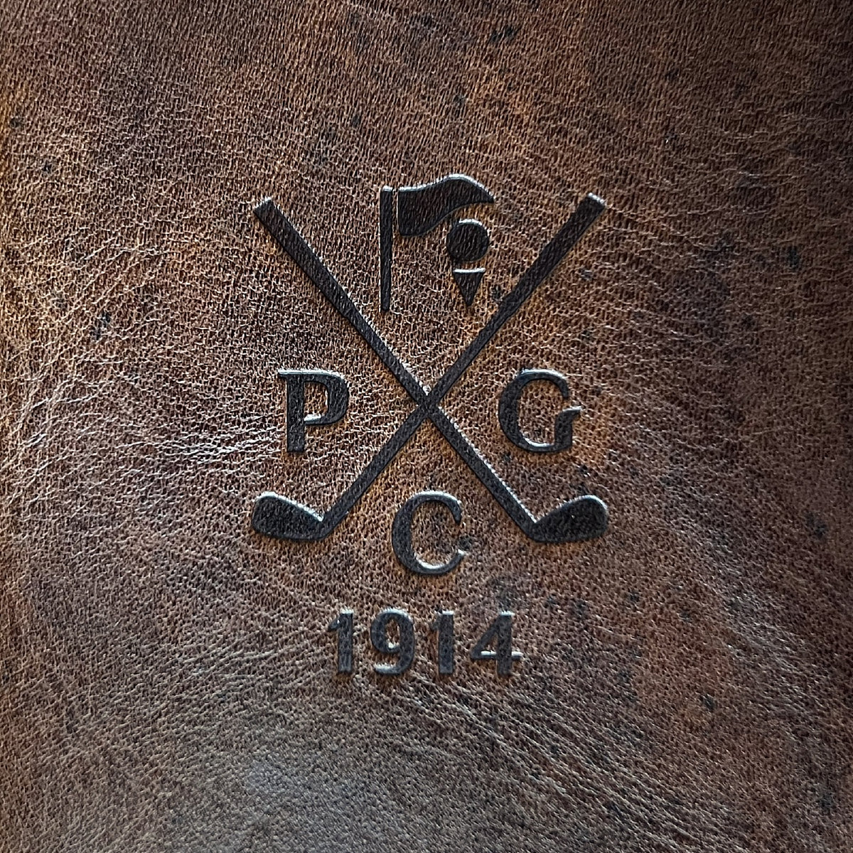 A golf club's crest debossed into a dark brown Nemesis leather yardage book cover, from a club order