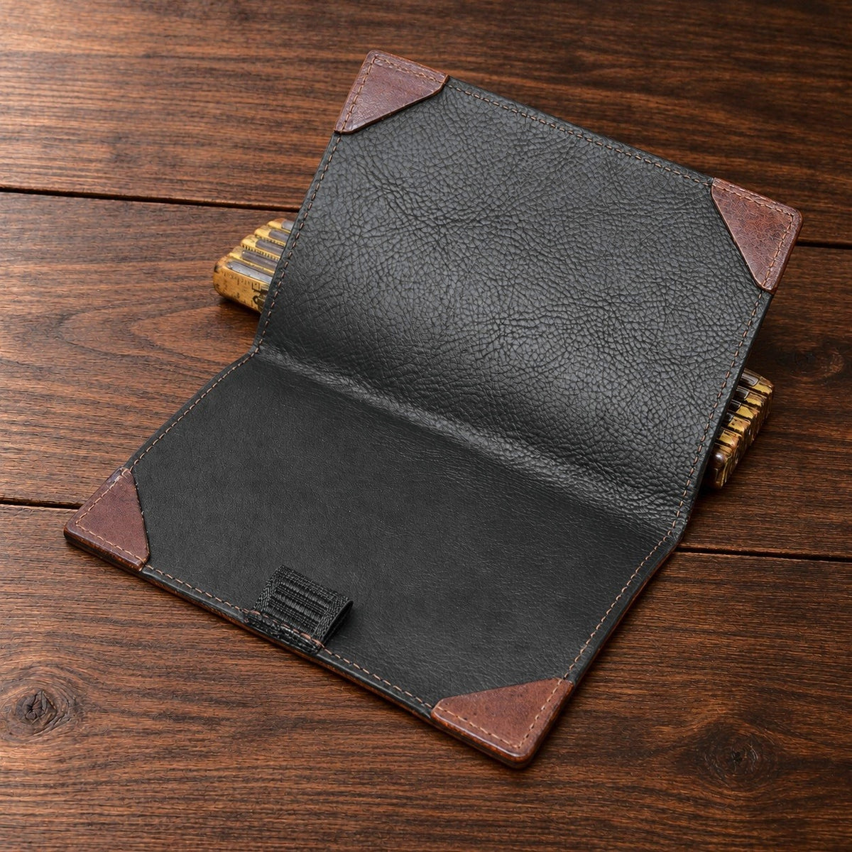 Inside of an open St. Andrews scorecard holder on a walnut table: black Minerva Box lining, brown leather corner pockets and a pencil loop