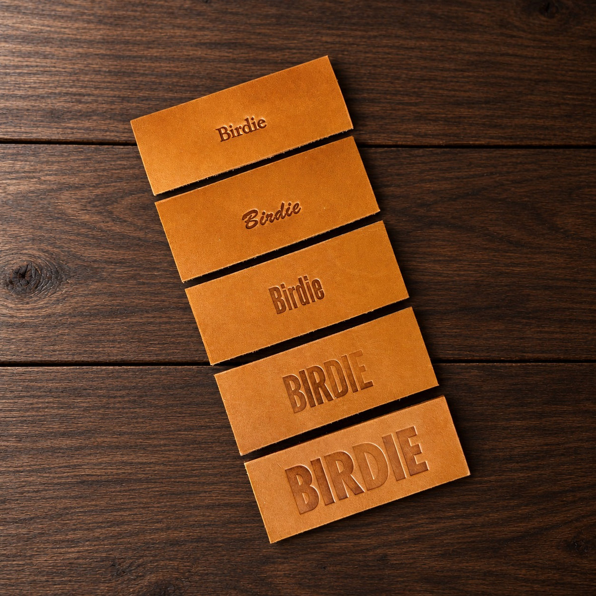 Five leather samples stamped Birdie in the five lettering styles, from top: Goudy, Brush, and Gothic in three sizes